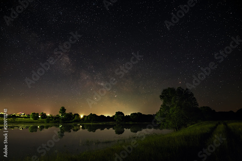 Space with stars in the night sky. The landscape with the river and trees is photographed on a long exposure.