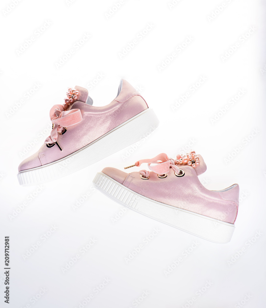 Footwear for girls and women decorated with pearl beads. Trendy sneakers  concept. Cute shoes isolated on white background, top view. Pair of pale  pink female sneakers with velvet ribbons. Stock Photo
