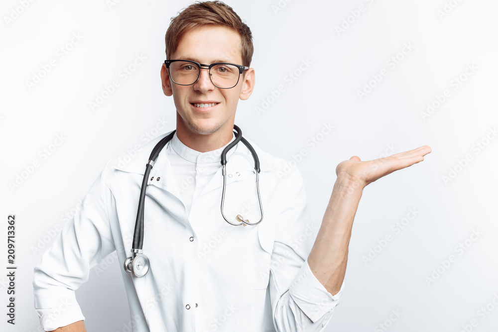 Portrait of a young doctor, on a white background, which points the hand to an empty view, trainee in the workshop, with a stethoscope on the neck, for advertising, text insertion