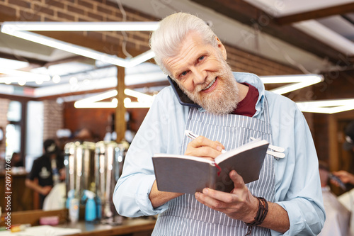 Being at work. Happy mature man looking forward, speaking with clients per telephone