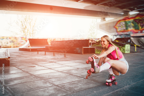 A picture of nice girl sitting in squat position. She is stretching her left leg and trying to keep balance. Girl is holding right hand on the edge of roller.