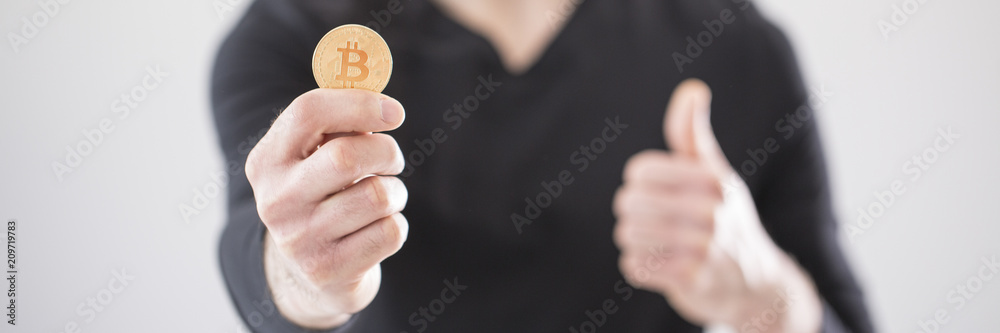 Close-up of a man holding a golden bitcoin cryptocurrency in his hand and blurry background with thumbs up pose Close-up of a man holding a golden bitcoin cryptocurrency in his hand and blurry background with thumbs up pose
