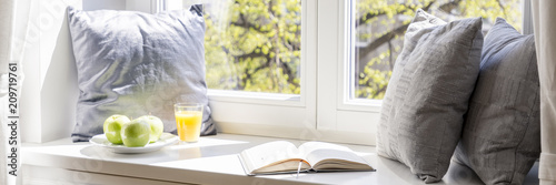 Billede på lærred Real photo of windowsill with three grey pillows, open book, green apples on pla