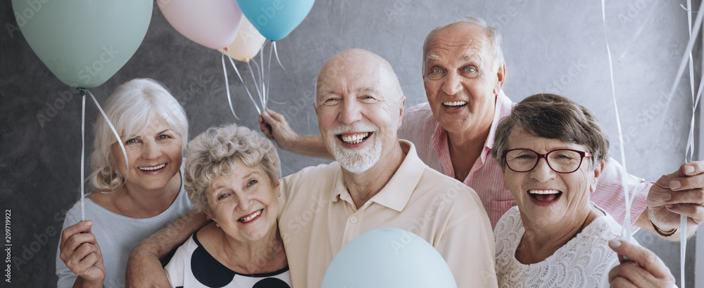 A group of happy, senior friends holding colorful balloons while posing at a party and celebrating birthday together. - obrazy, fototapety, plakaty 