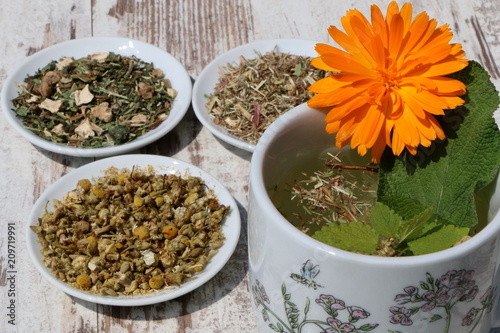 Herbal Tea, Kräutertee, Teetasse mit Kräutertee (Ringelblume, Salbei, Melisse) und daneben eine Auswahl traditioneller getrockneter Heilkräuter für Gesundheitsteemischungen