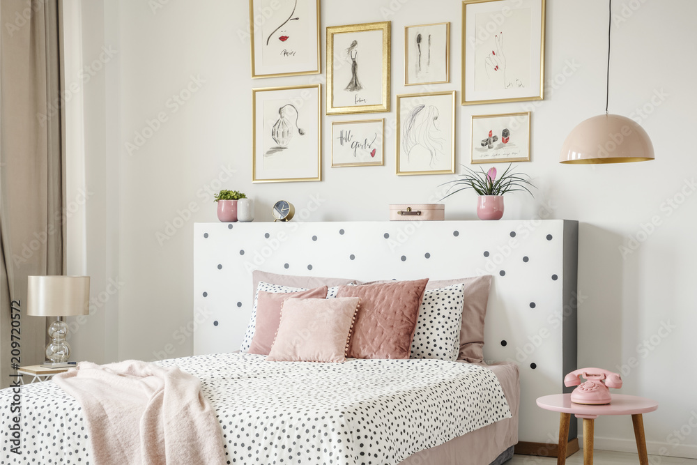 Beautiful white bedroom interior with feminine decor, polka dot pattern, pink accessories and framed sketches gallery on the wall - obrazy, fototapety, plakaty 