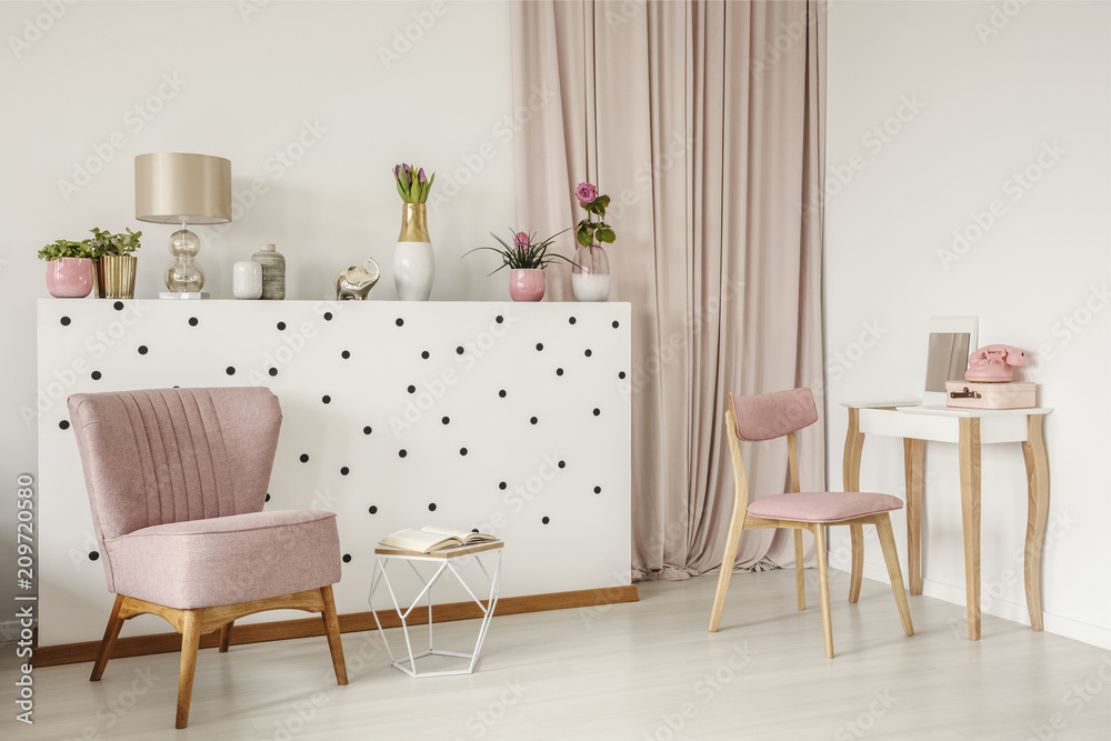 Elegant armchair and an open book by a polka dot wall, wooden vanity and curtains in a white bedroom interior with dirty pink elements - obrazy, fototapety, plakaty 
