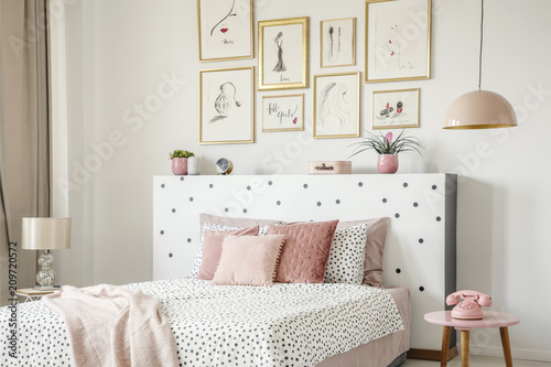 Beautiful white bedroom interior with feminine decor, polka dot pattern, pink accessories and framed sketches gallery on the wall photo