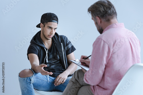 Tableau sur toile Rebellious spanish man talking to professional psychologist during meeting