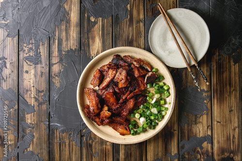 Chinese traditional dish Cantonese BBQ Pork Belly with spring onion served in ceramic plate with chopsticks over dark wooden plank background. Flat lay, space. Asian style dinner.