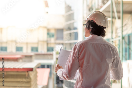 Engineer or Architect checking architectural drawing while wearing a personal protective equipment safety helmet at construction site. Engineering, Architecture and construction business concepts