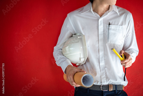 Engineer or Architect holding protective safety helmet, tape measure and architectural drawing in red background. Engineering, Architecture and building construction business concepts