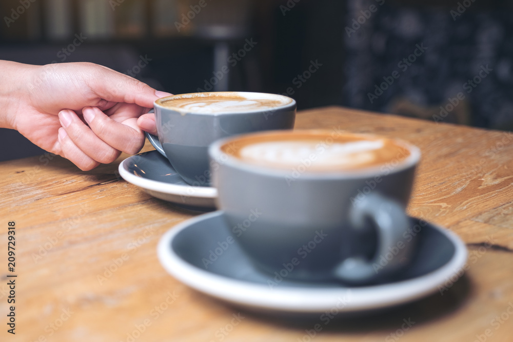 Closeup image of a hand holding blue cup of hot latte coffee on vintage wooden table in cafe