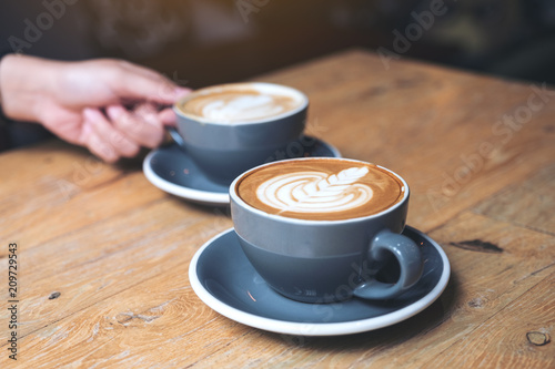 Closeup image of a hand holding blue cup of hot latte coffee on vintage wooden table in cafe