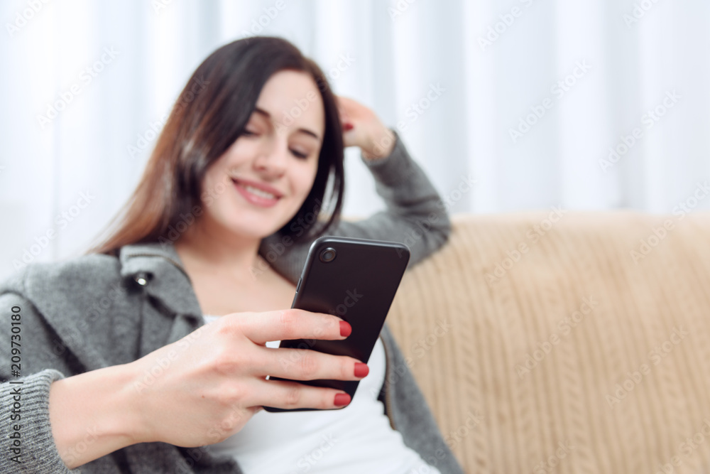 young woman communicates with each other through a cellphone sitting on a sofa young woman communicates with each other through a cellphone sitting on a sofa