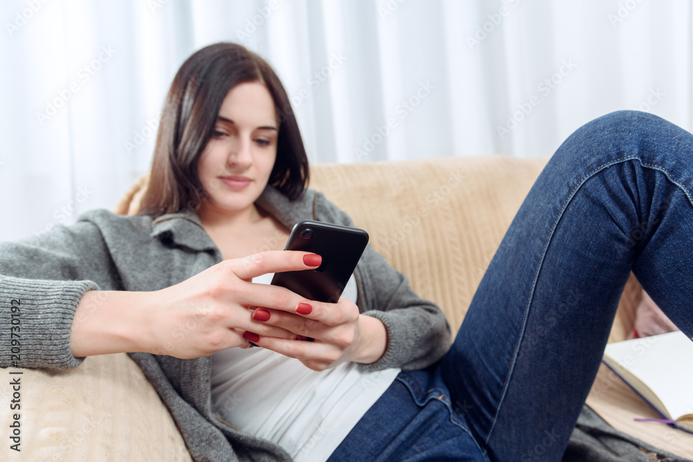 young woman communicates with each other through a cellphone sitting on a sofa young woman communicates with each other through a cellphone sitting on a sofa