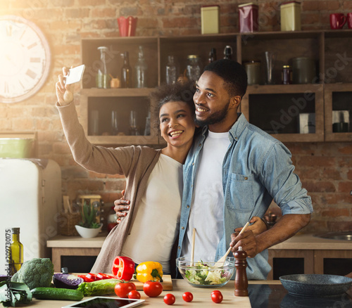 Happy black couple taking selfie at kitchen