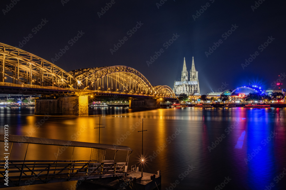 Fototapeta premium Hohenzollernbrücke, Kölner Dom und Musical Dome mit Anlegesteg für die Fähre - Panorama bei Nacht