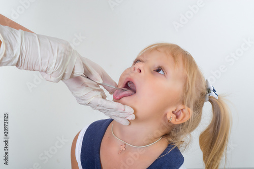 The doctor examines the throat of a little girl. At the reception of a pediatrician. Throat diseases.