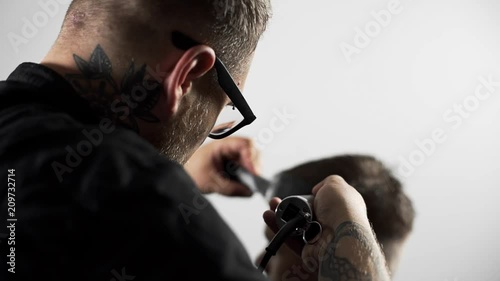 Tattoed barber makes haircut for customer at the barber shop by using hairclipper, man's haircut and shaving at the hairdresser, barber shop photo