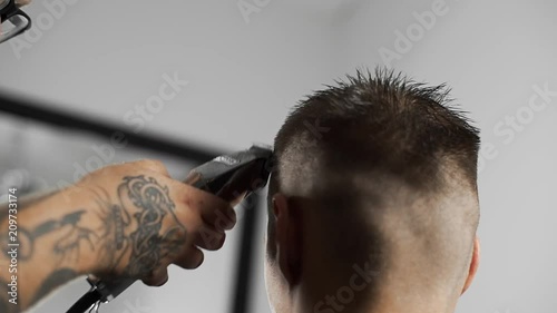 Tattoed barber makes haircut for customer at the barber shop by using hairclipper, man's haircut and shaving at the hairdresser, barber shop photo