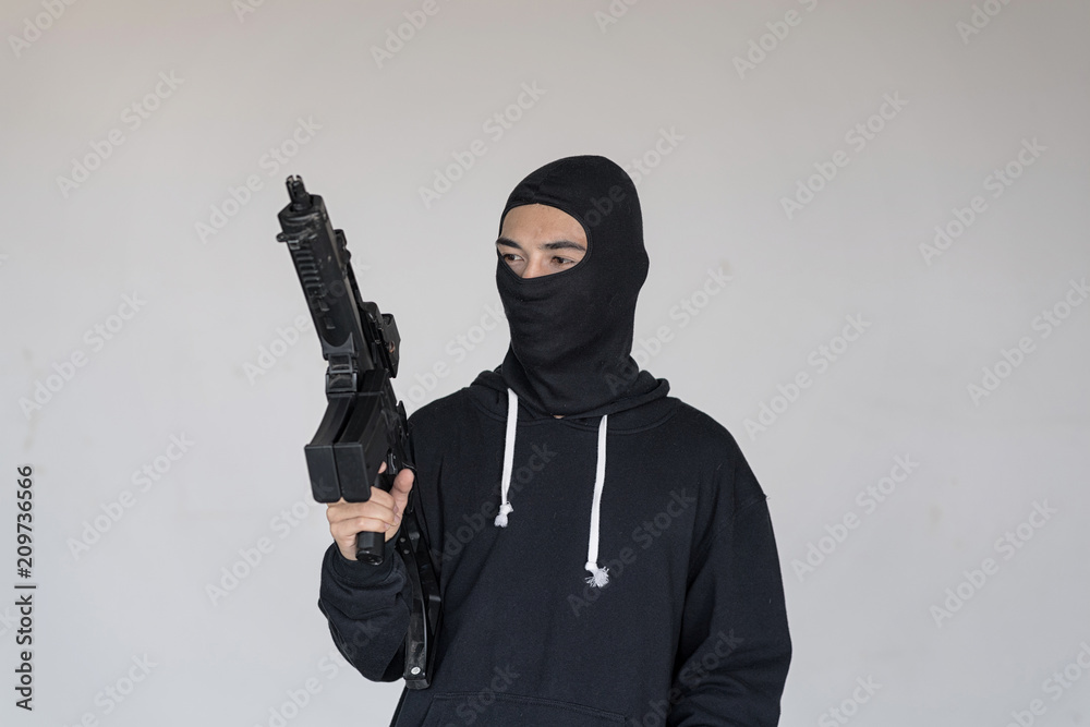 Black masked Robber in the black long sleeve shirt is holding the machine gun in his hand. He look at the gun. Black masked Robber in the black long sleeve shirt is holding the machine gun in his hand. He look at the gun.