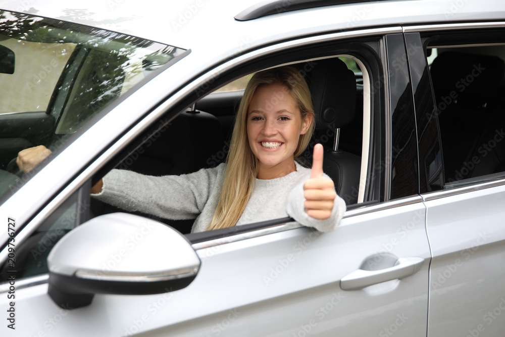 Hübsche blonde Frau am Steuer eines Autos lächelt und zeigt Daumen hoch Hübsche blonde Frau am Steuer eines Autos lächelt und zeigt Daumen hoch
