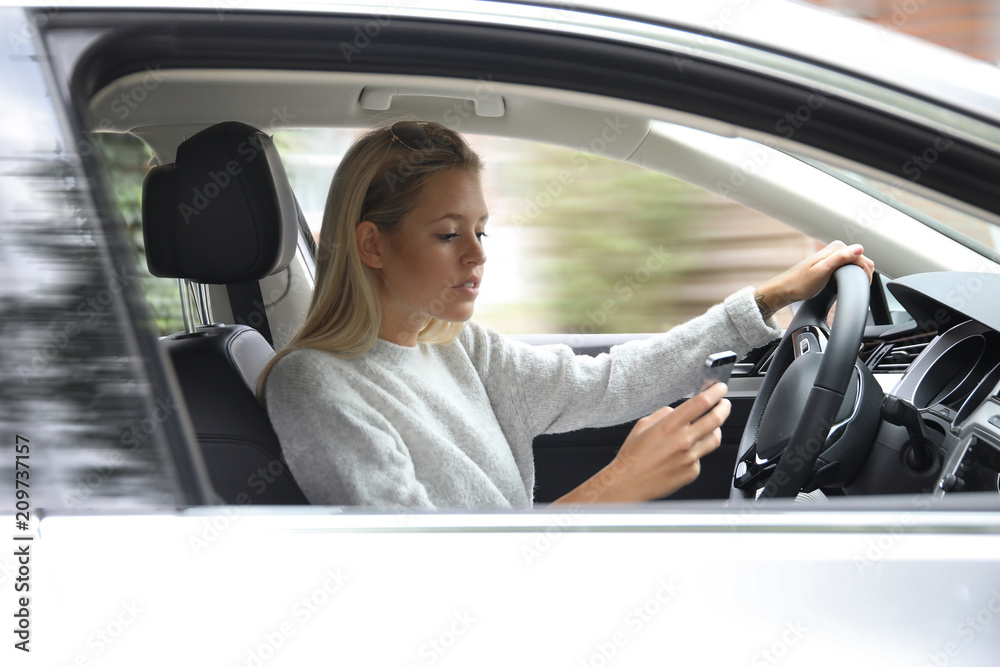 Hübsche blonde Frau schaut auf ihr Handy während des Autofahrens