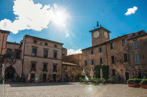 Square with old buildings, clock tower, shop and sunny sky in Orvieto, a pleasant and well preserved medieval town. Located in Umbria, central Italy. Retouched photo