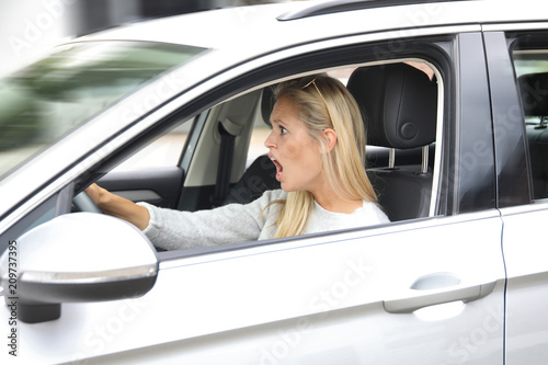 Hübsche blonde Frau steuert ein Auto und schaut entsetzt nach vorne