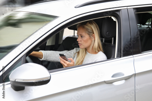 Hübsche blonde Frau steuert ein Auto und hält ein Smartphone in den Händen © Joerch