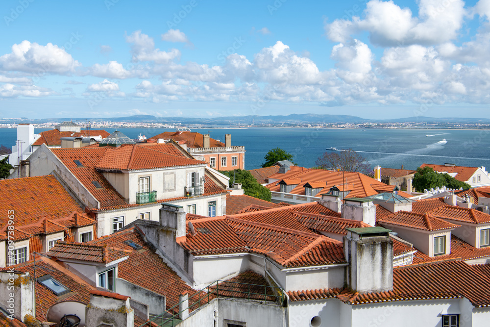 View over the red tile roofs of the Alfama district under a beautiful blue sky with puffy white clouds in Lisbon, Portugal