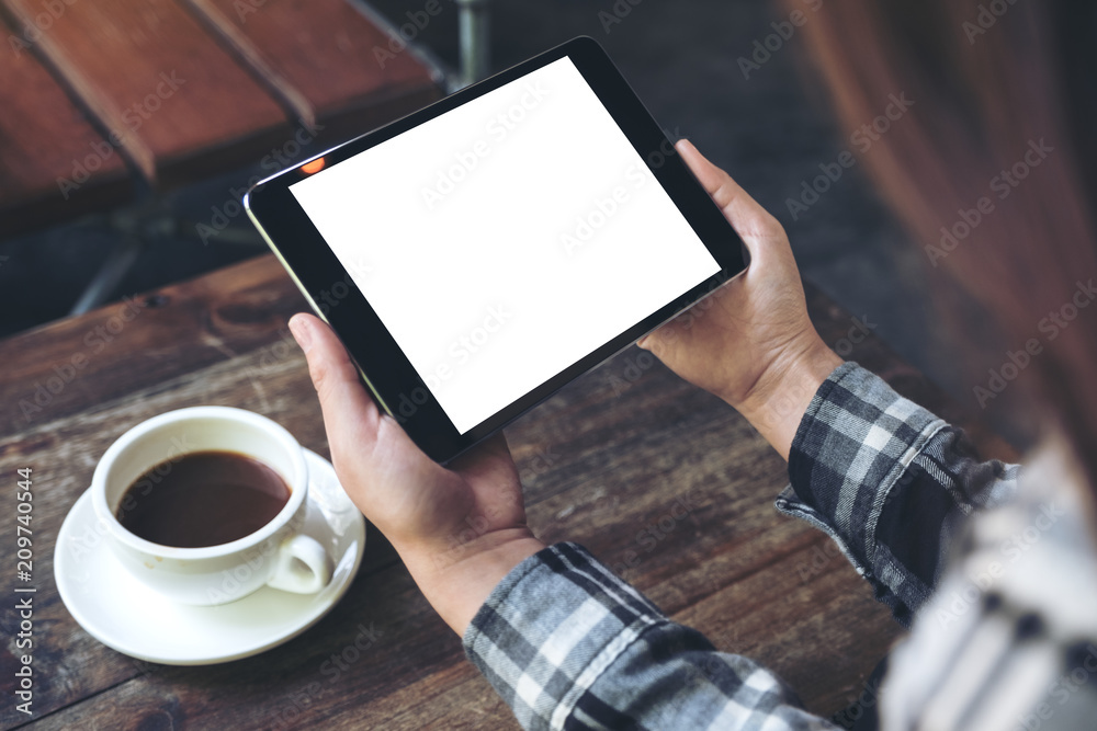 Mockup image of a woman holding black tablet pc with white blank screen with coffee cup on table background Mockup image of a woman holding black tablet pc with white blank screen with coffee cup on table background