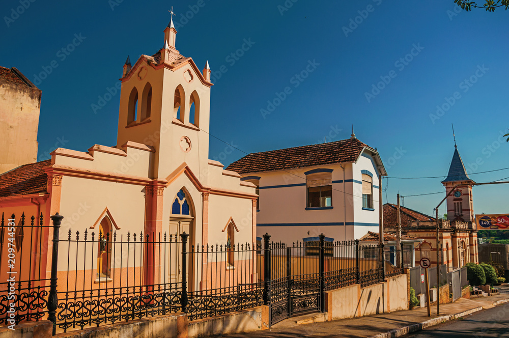 Facade of small church and belfry behind iron fence, in a sunny day at São Manuel. A cute little town in the countryside of São Paulo State. Retouched photo.