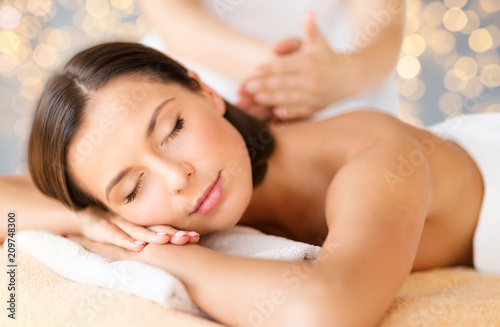 wellness  spa and beauty concept - close up of beautiful woman having massage over holidays lights background