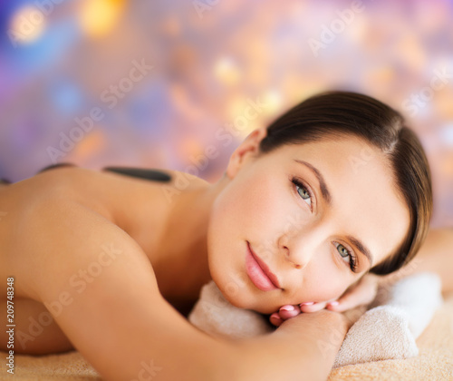 wellness  spa and beauty concept - beautiful woman having hot stone therapy over holidays lights background
