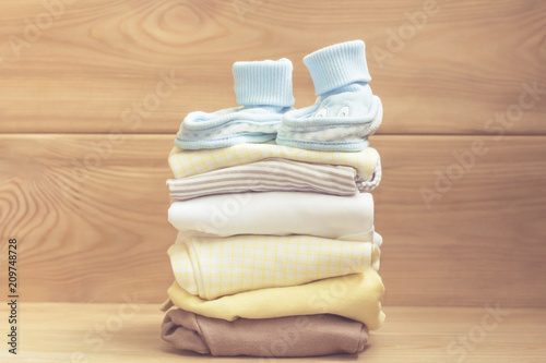 blue baby shoes on clothes stack. Pastel clothes for baby infant on wooden background. Newborn.