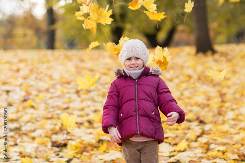 childhood  season and people concept - happy little girl playing with fallen leaves at autumn park