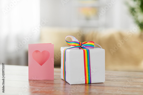 homosexual and lgbt concept - gift box with gay pride awareness ribbon and greeting card on wooden table at home