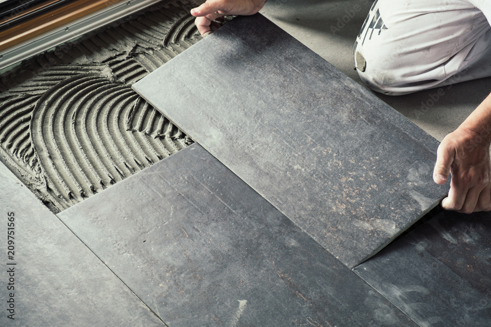 Worker placing dark grey ceramic floor tiles on adhesive surface - obrazy, fototapety, plakaty 
