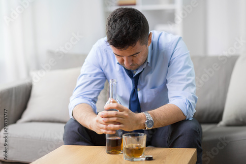 alcoholism, alcohol addiction and people concept - male alcoholic with bottle and drinking whiskey at home photo