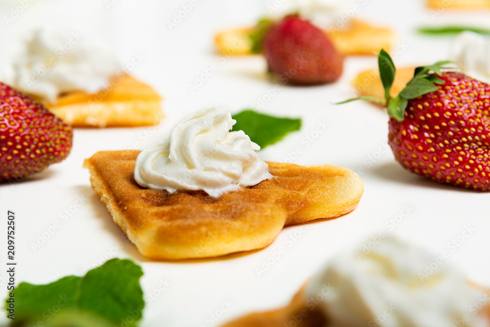 Close-up of a heart shaped waffle decorated with cream, strawberries and mint leaves on white background. Close-up of a heart shaped waffle decorated with cream, strawberries and mint leaves on white background.