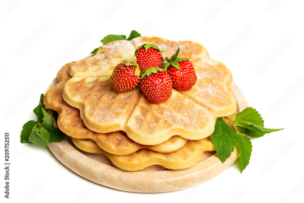 A pile of sugar waffles decorated with strawberries and mint leaves on a wooden board. A pile of sugar waffles decorated with strawberries and mint leaves on a wooden board.