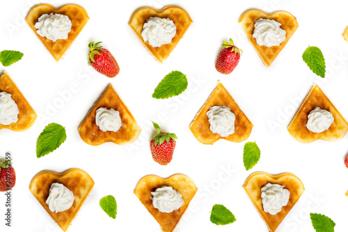 Heart shaped waffles served with cream, strawberries and mint leaves forming an abstract pattern on white background.
