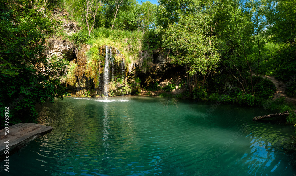 Naklejka premium Waterfall and a beautiful lagoon lake for relaxing in the summer forest.