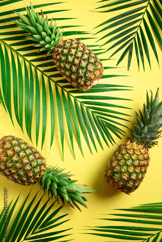 Pineapple and tropical palm leaves on yellow background. Top view. Summer concept. Creative flat lay with copy space.