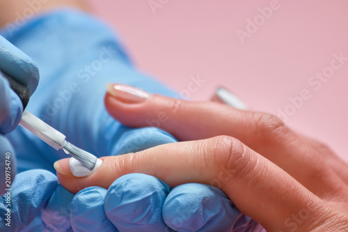 Painting female nails with white. Manicurist treating a client at beauty salon. Beautician painting nails.