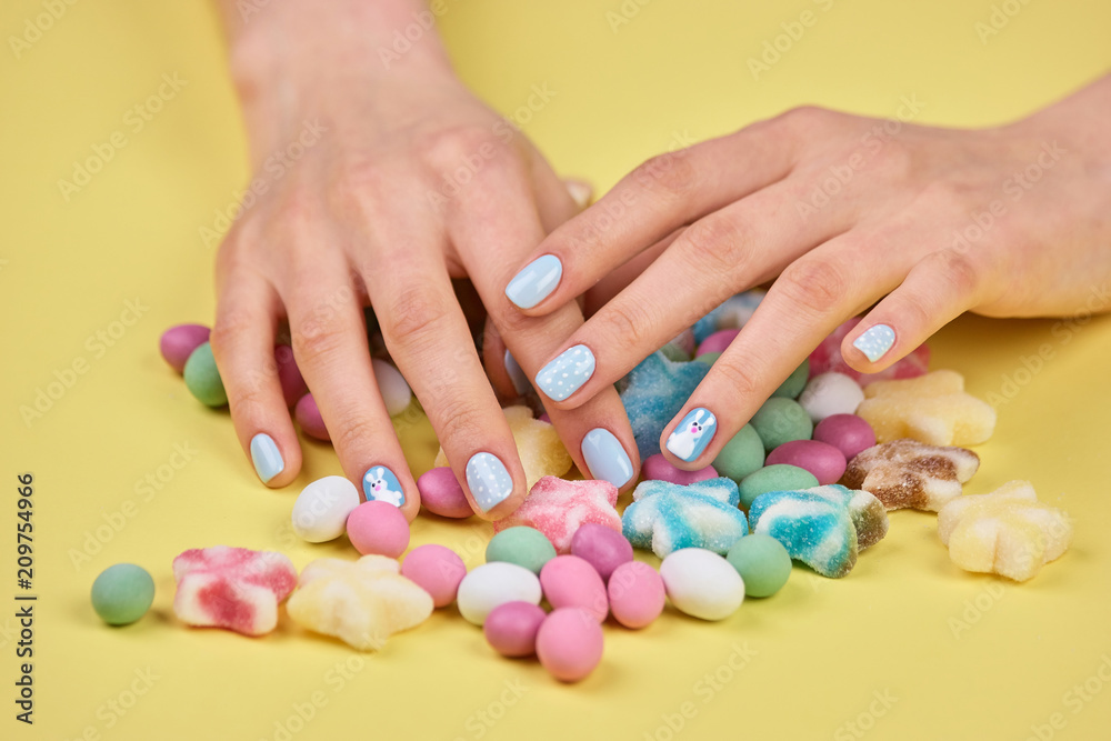 Woman hands on colorful candies. Bright delicious candies and female manicured hands on yellow background.