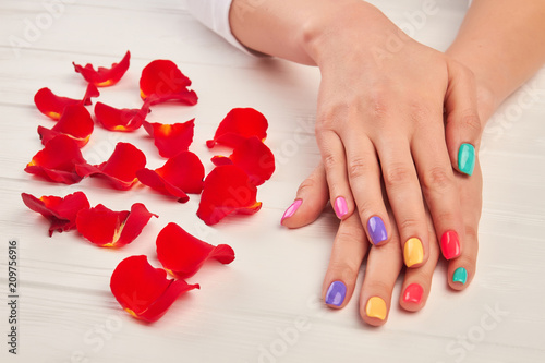 Woman manicured hands in spa salon. Young woman hands with colorful varnish on nails, white wooden background. Beautiful summer manicure and rose petals decorations. photo