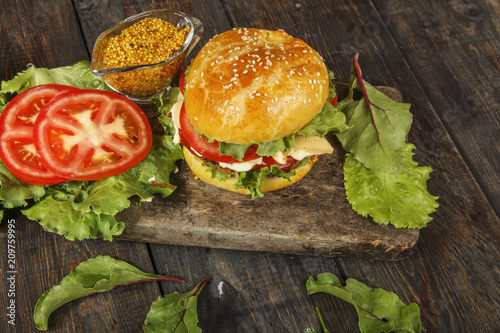 Hamburger on a wooden board against a dark background with copy space. Hamburger with sauce and fresh vegetables on a wooden table. Burger.